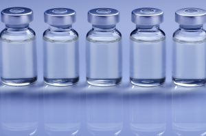 Vials with liquid drug as vaccine dose flu shot for injection treatment on medical table. Vaccination or immunization care concept background.