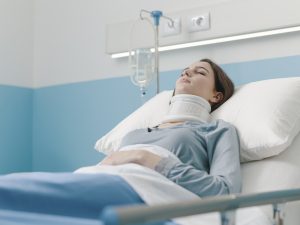 Young woman lying in a hospital bed with IV drip and a cervical collar, she is hospitalized after a serious accident